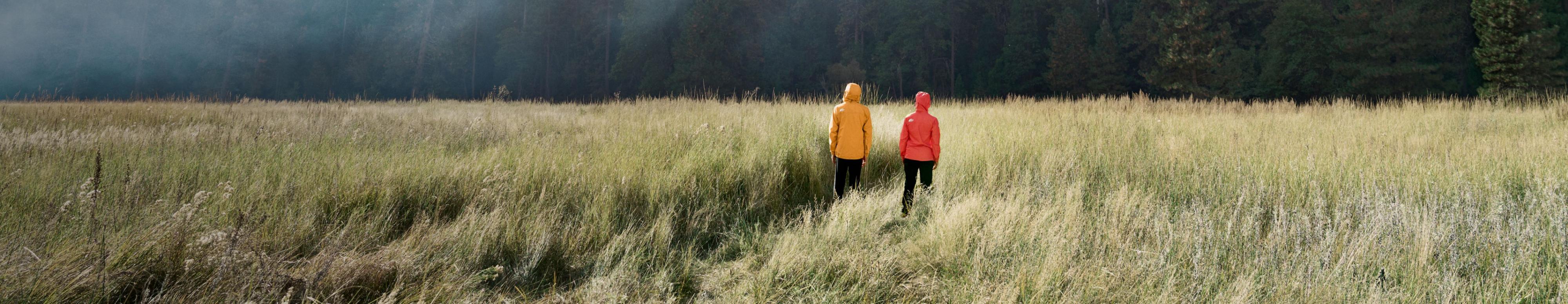 Two people are standing in a grassy field, with their hoods up, wearing rain coats from The North Face. Text reads: “Wind. Rain. We’ve got you covered.” 