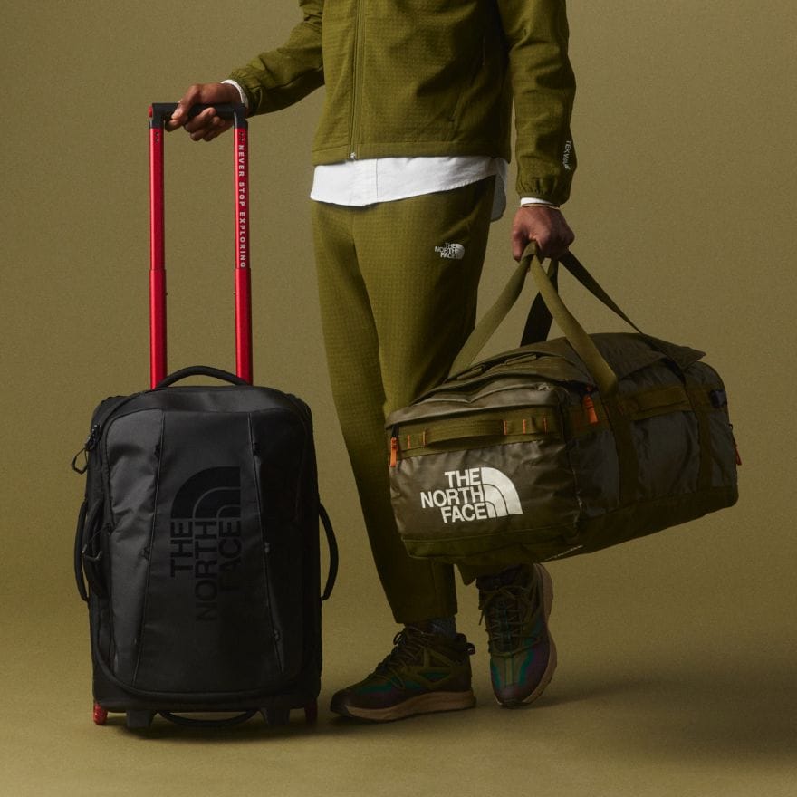 A person carrying a rolling suitcase and duffel bag from The North Face. 