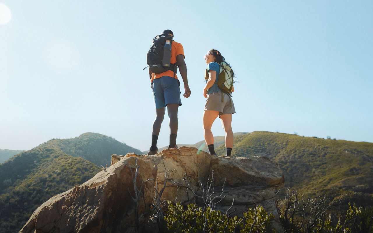It’s a sunny day and two people are at the summit of the mountain wearing backpacks and other hiking gear from The North Face. Text reads: “On the trail. In your element.”