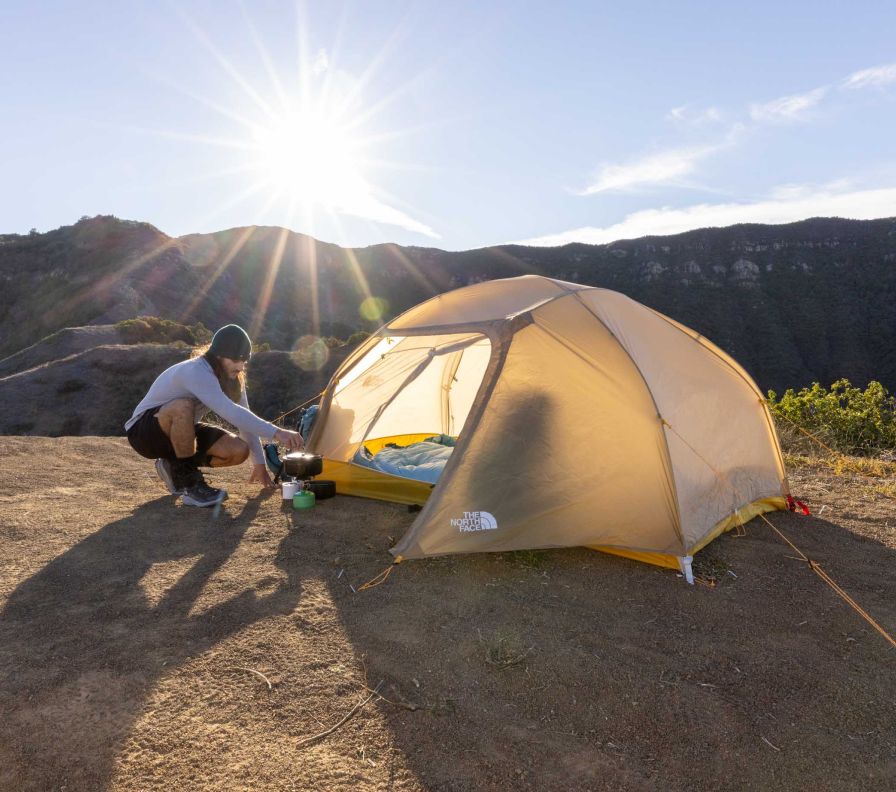 Une personne cuisine sur son réchaud de camping devant sa tente The North Face. 
