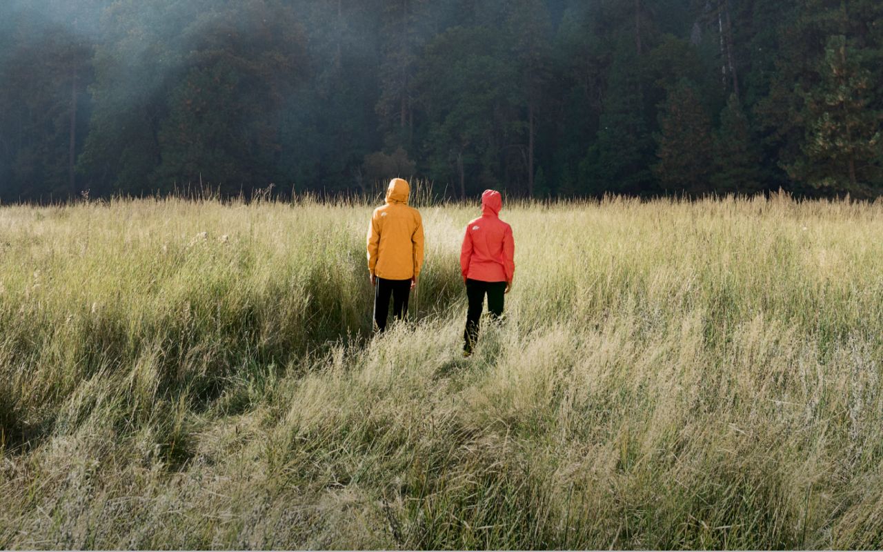 Deux personnes se tiennent dans un champ herbeux, capuches relevées, vêtues de manteaux imperméables de la marque The North Face. La mention suivante y est inscrite : « Wind. Rain. We’ve got you covered ». 