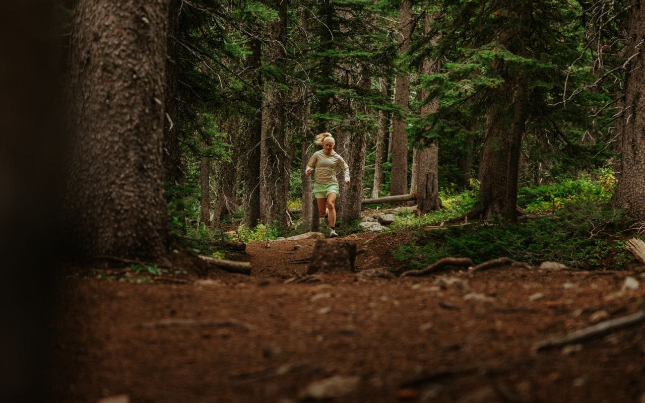 Une femme fait de la course sur sentier dans les bois vêtue d’une tenue de la marque The North Face. La mention suivante y est inscrite : « Cutting-edge comfort, from road to ridge ». 