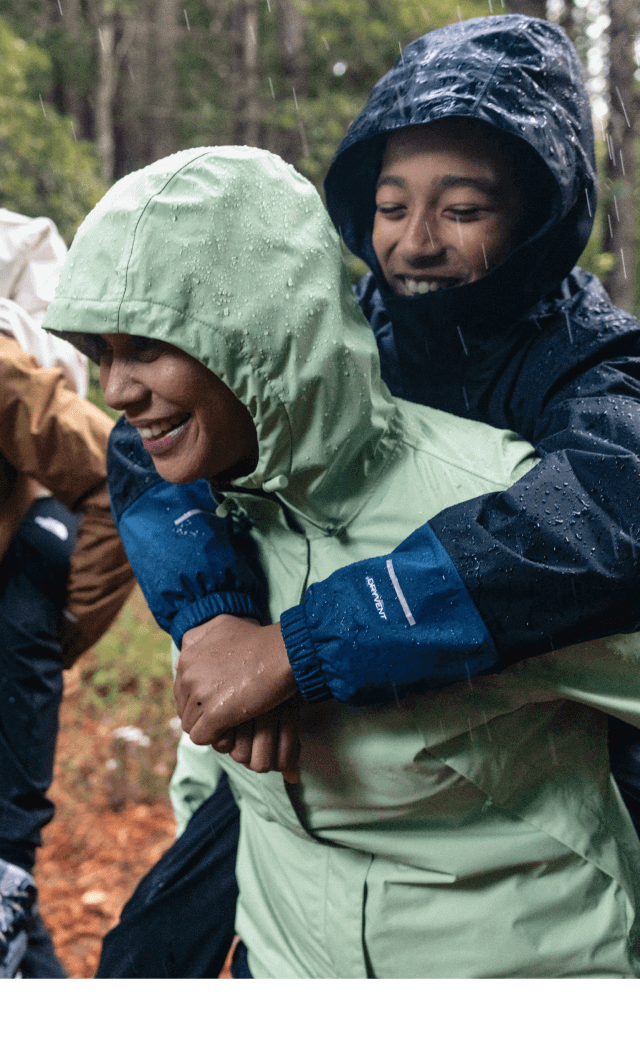 Parents give their kids a piggyback ride along a rainy trail while wearing waterproof jackets.  