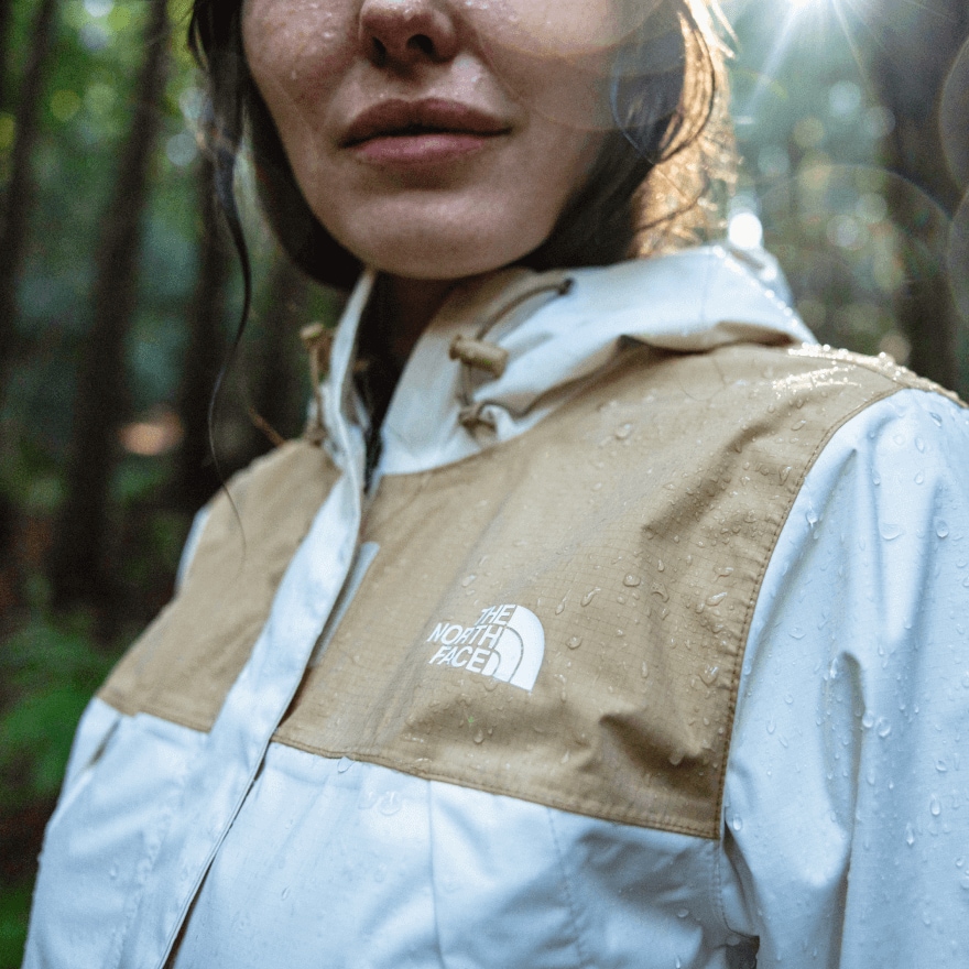 A woman walks through a rainy forest as droplets shed off her waterproof jacke