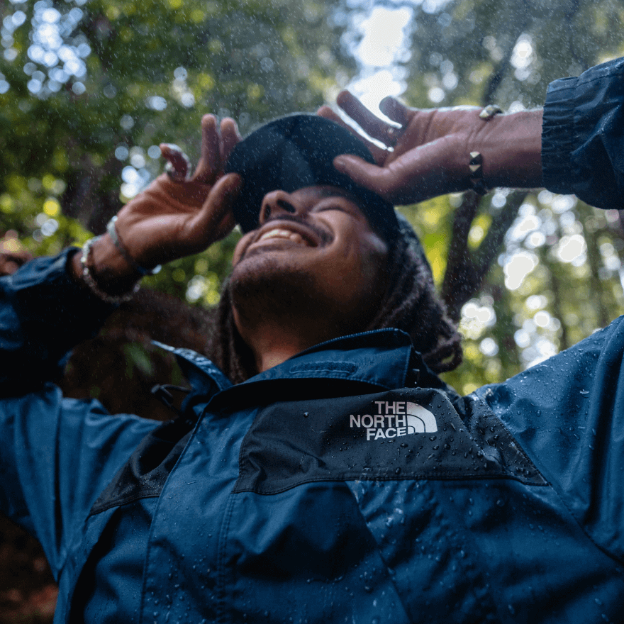 A man wearing a waterproof jacket smiles while embracing a rain shower. 