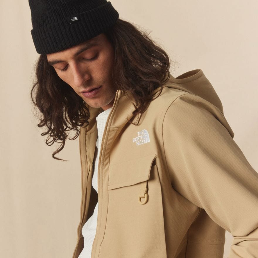 A man is looking down wearing the Willow Stretch Hoodie in Khaki Stone and a black beanie. 