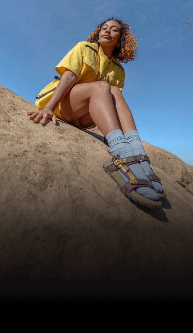 Explore Fund council member Evelynn Escobar is wearing yellow gear from The North Face Hike Clerb Capsule Collection as she runs across cliffs on under a blue sky. 