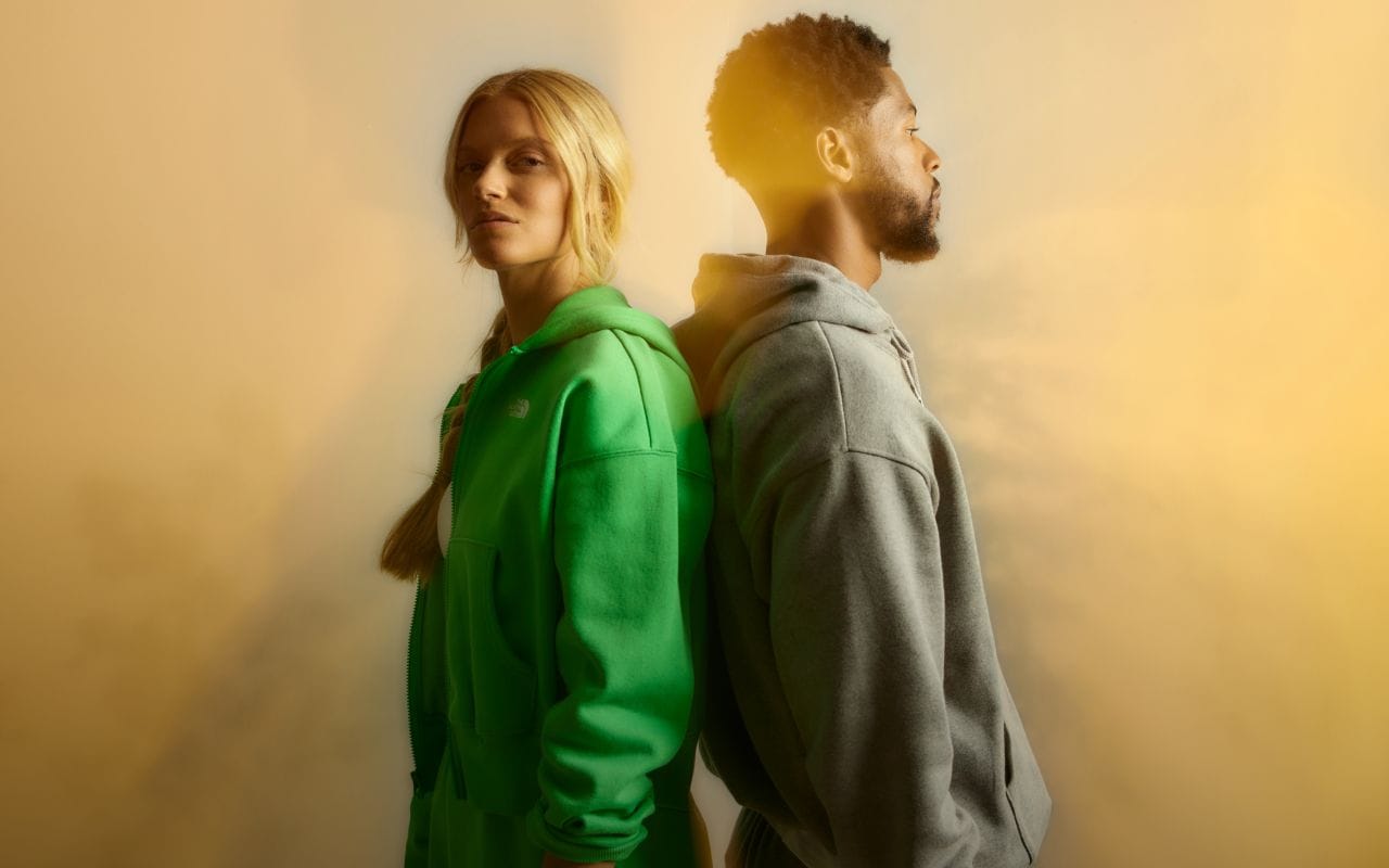 A studio shot of a man and woman standing back-to-back while wearing hoodies.