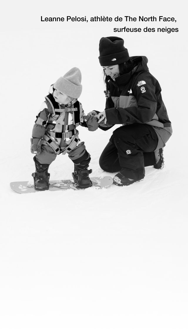 Image en noir et blanc de l’athlète de The North Face, Leanne Pelosi, agenouillée dans la neige, aidant son enfant à enfiler son habit de neige.