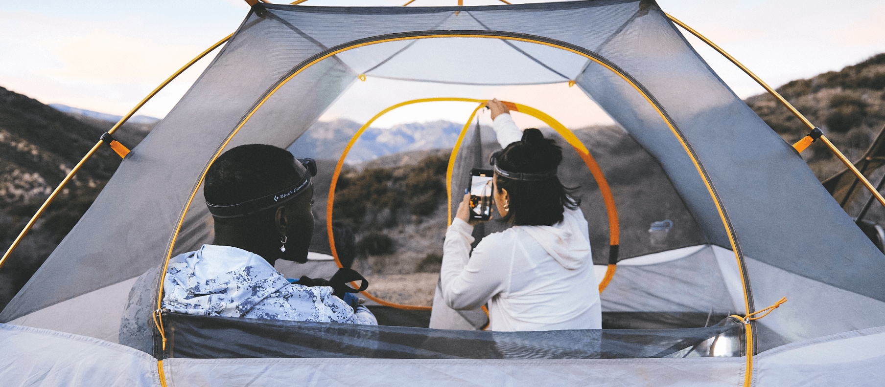 Two people sit in a tent from The North Face with their backs to the camera.  