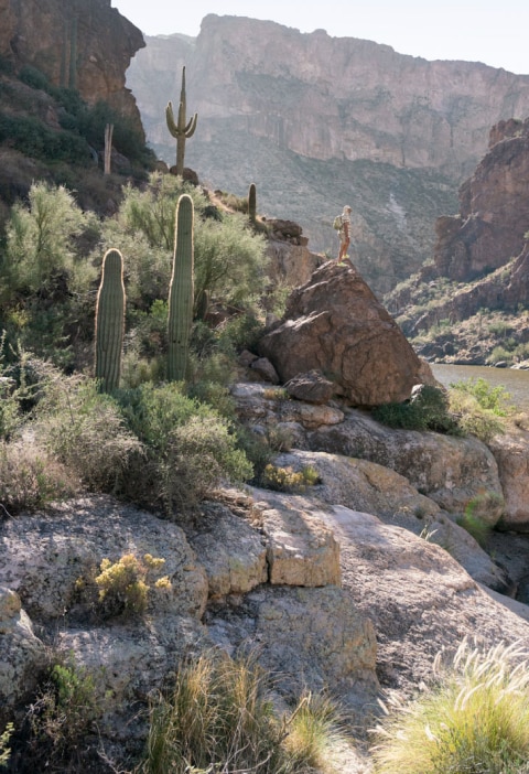 Person standing atop a rock in the desert, overlooking river. 