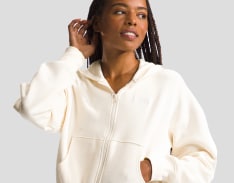 Woman in a white zip-up sweatshirt, tucking hair behind ear.