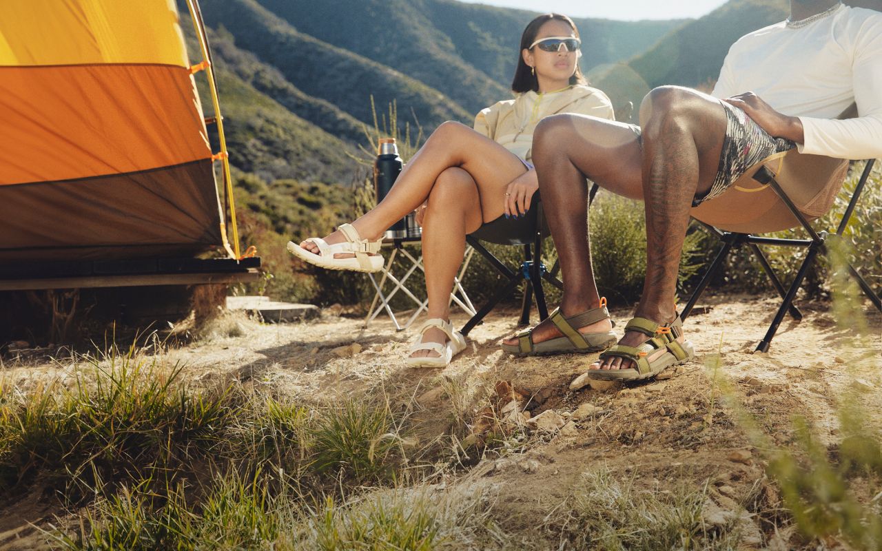 Un homme et une femme portant des sandales de la marque The North Face sont assis sur des chaises de camping dans un décor de montagne désertique.