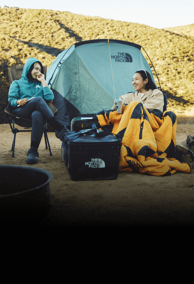 Two friends share a laugh while sitting outside of their Wawona Tent at a campsite.