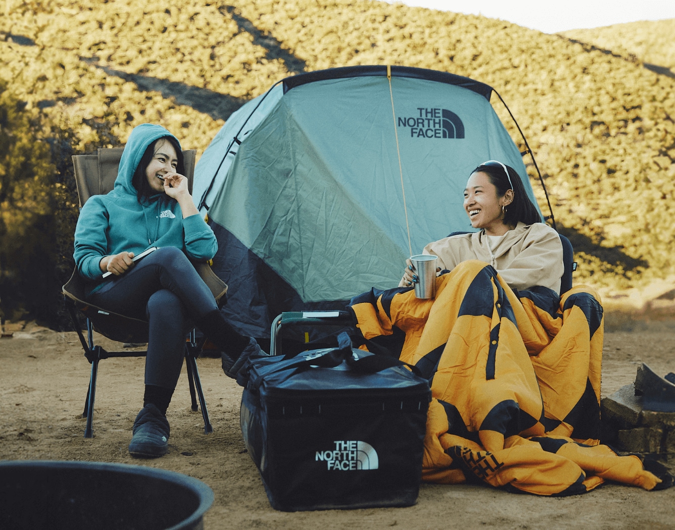 Two friends share a laugh while sitting outside of their Wawona Tent at a campsite. 